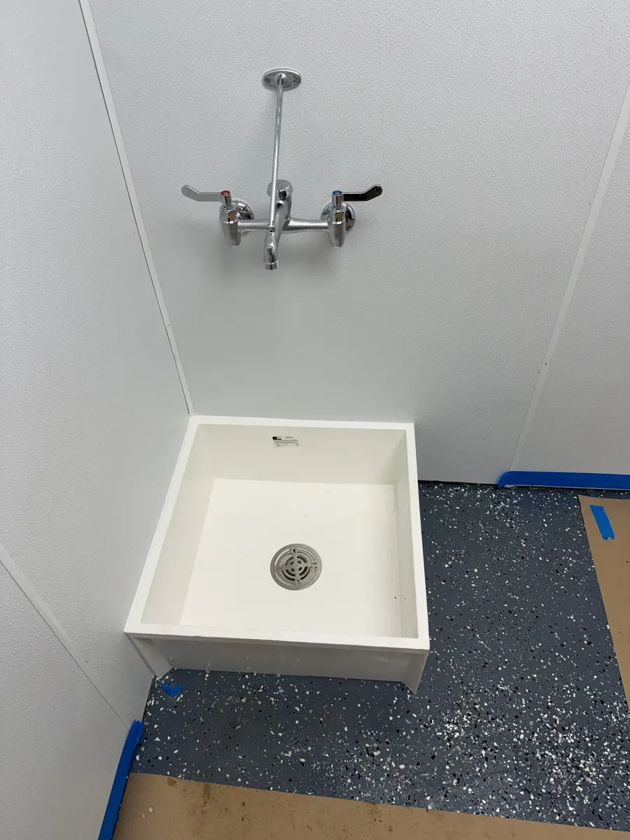 A white floor-mounted mop sink set in the corner of a commercial utility room with a chrome wall-mount service faucet above it