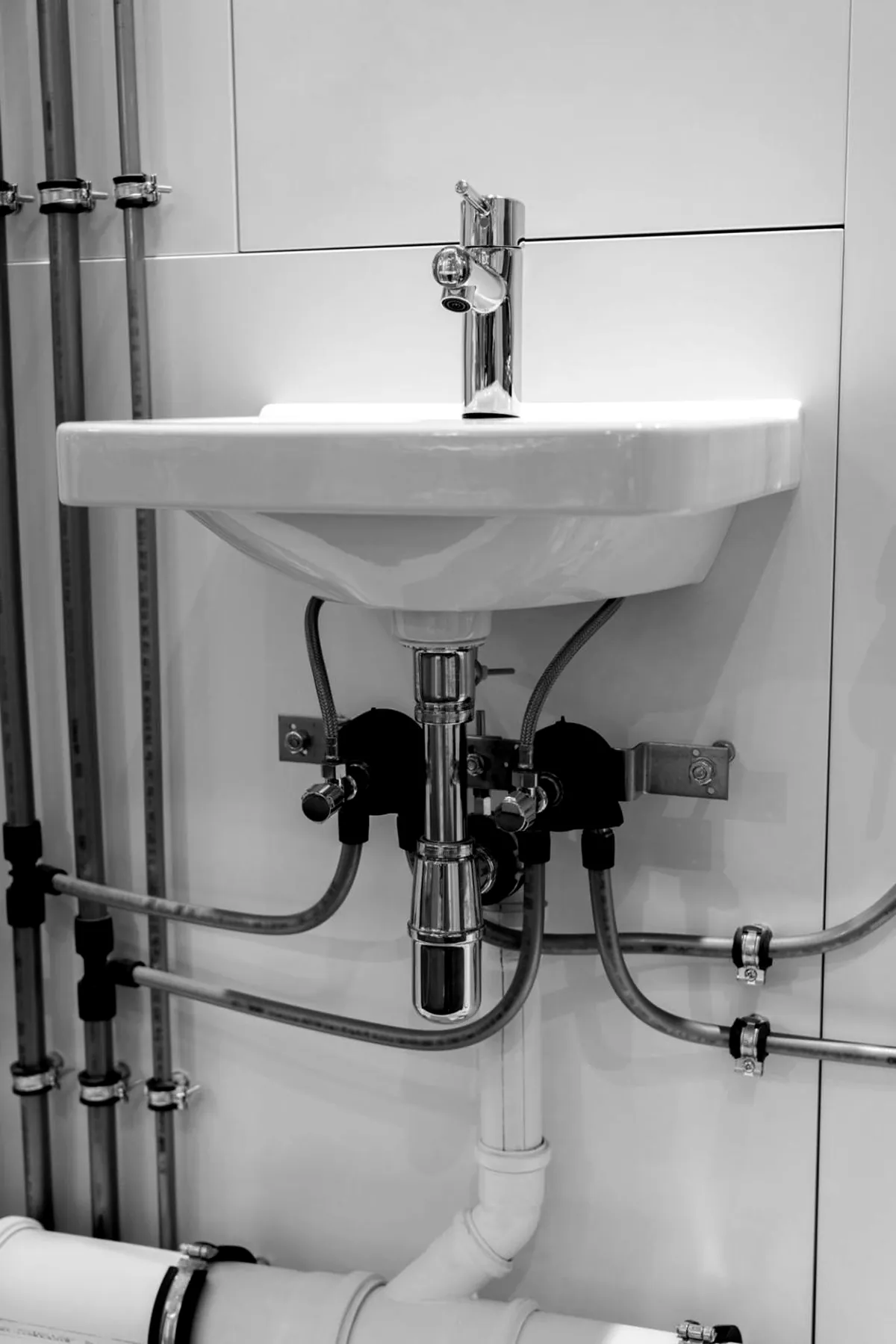 Wall-hung sink rough-in with chrome supply valves, trap, and exposed supply lines run to the wall
